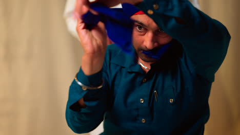 Fotografía-De-Estudio-De-Un-Hombre-Sikh-Mayor-Que-Ayuda-A-Un-Hombre-Sikh-Más-Joven-A-Atar-La-Tela-Para-Un-Turbante-Contra-Un-Fondo-Liso,-Filmada-En-Tiempo-Real-3